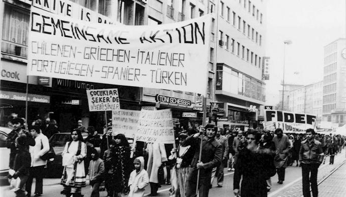 Eine der Migrant:innen-Demonstrationen, vor deren Hintergrund die Föderation der Immigrantenvereine aus der Türkei (FIDEF) zu sehen ist. (Der Ort, die Demonstration und der Besitzer des Fotos sind unbekannt). Quelle: Domid.org