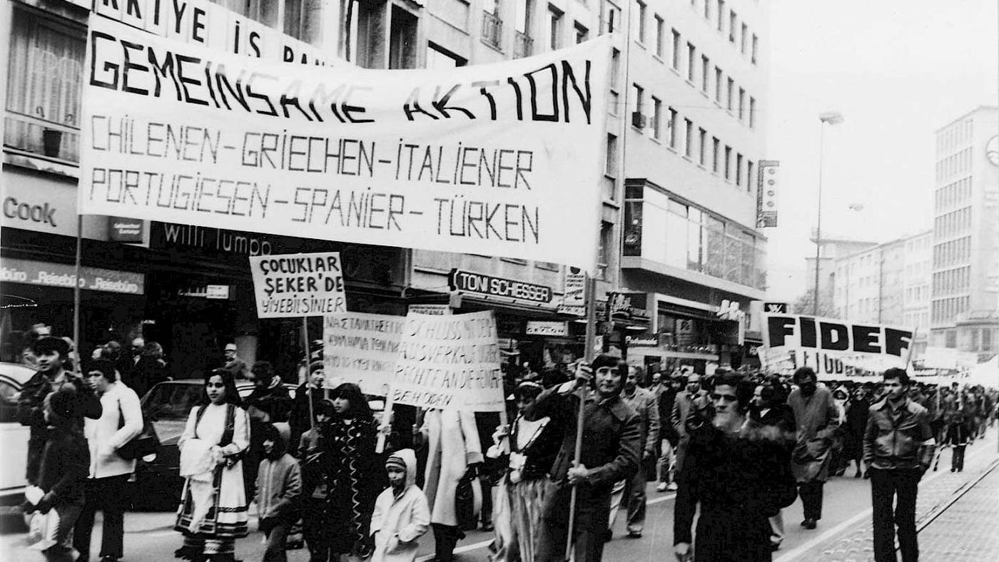 Eine der Migrant:innen-Demonstrationen, vor deren Hintergrund die Föderation der Immigrantenvereine aus der Türkei (FIDEF) zu sehen ist. (Der Ort, die Demonstration und der Besitzer des Fotos sind unbekannt). Quelle: Domid.org